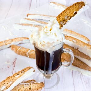 Almond biscotti dunked into a cup of coffee topped with whipped cream